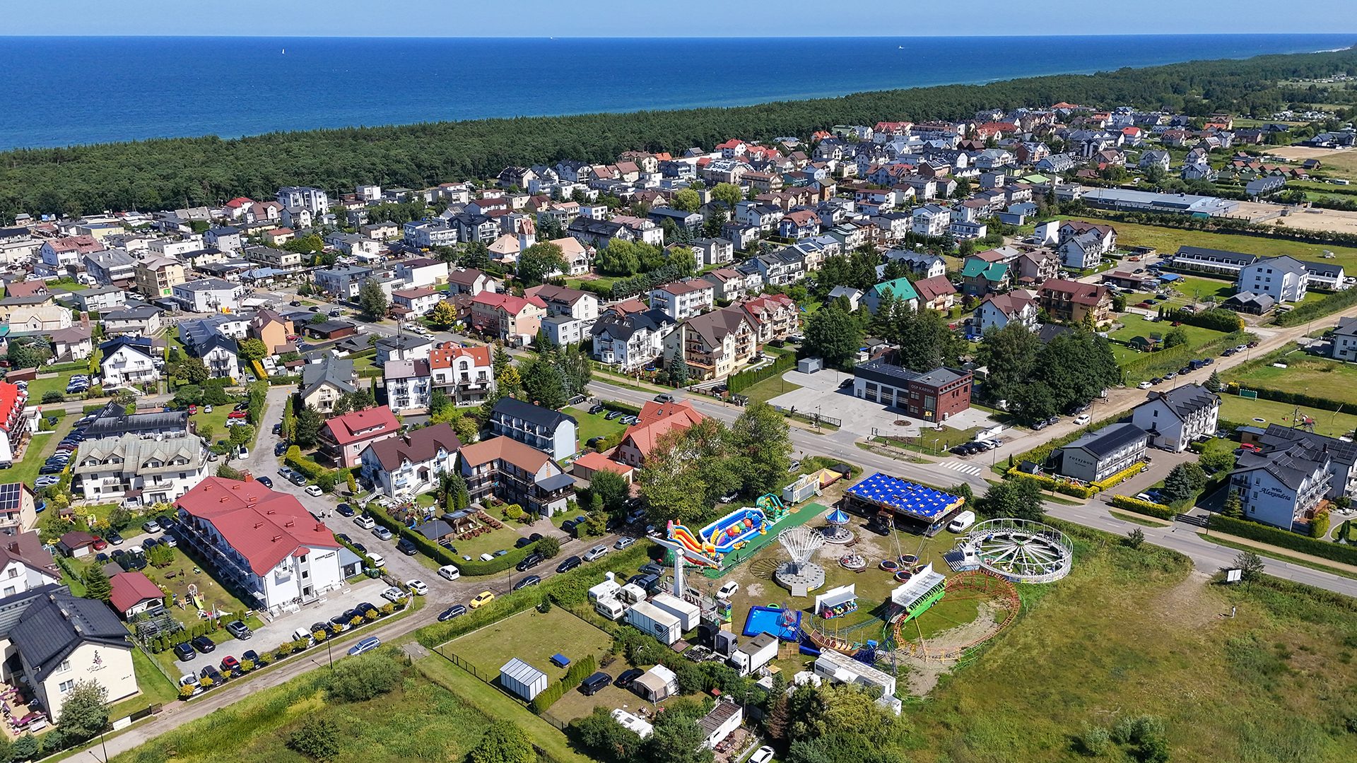 Karwia z lotu ptaka — pensjonaty i domy wczasowe nad Morzem Bałtyckim, pas nadmorskiego lasu i plaża na horyzoncie